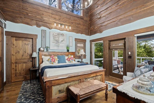 bedroom with access to exterior, a notable chandelier, a high ceiling, and wood finished floors