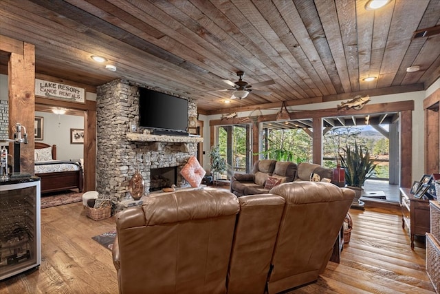 living area featuring light wood-type flooring, wooden ceiling, ceiling fan, and a stone fireplace