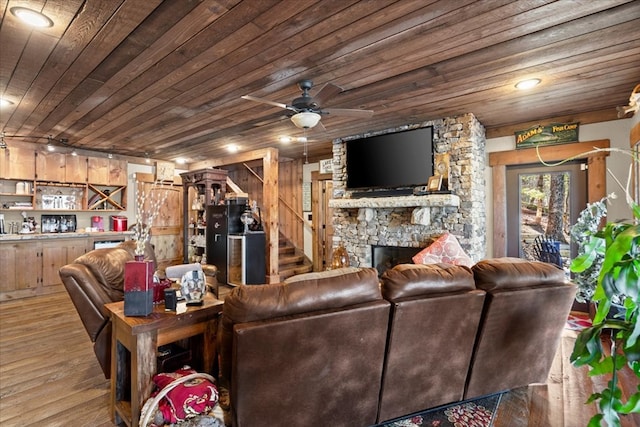 living room with light wood finished floors, wood ceiling, a stone fireplace, a bar, and stairs