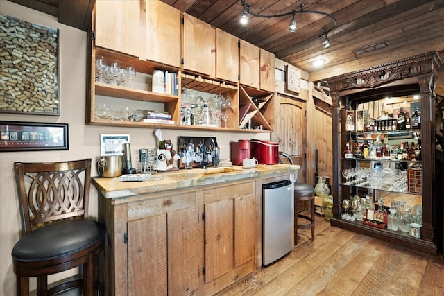 bar with light wood-style floors, freestanding refrigerator, and a bar