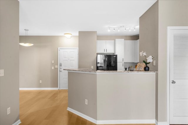 kitchen with black fridge, light stone counters, decorative light fixtures, light hardwood / wood-style flooring, and white cabinets