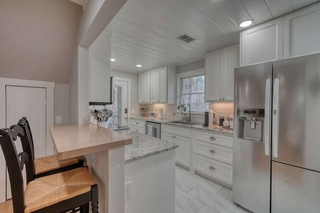 kitchen with a kitchen bar, sink, light stone counters, appliances with stainless steel finishes, and white cabinets