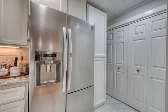 kitchen with white cabinetry, stainless steel fridge, light stone counters, and backsplash