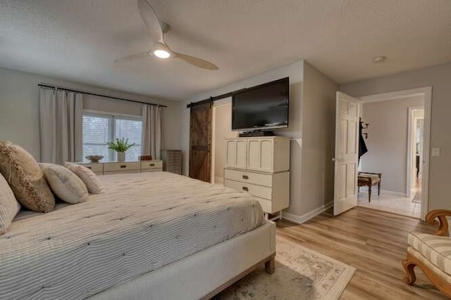 bedroom featuring ceiling fan, a barn door, a textured ceiling, and light wood-type flooring