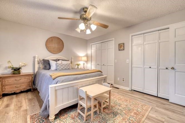 bedroom featuring multiple closets, ceiling fan, light hardwood / wood-style flooring, and a textured ceiling