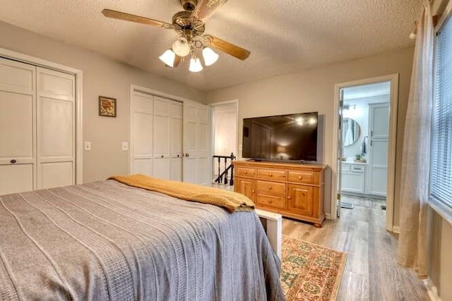 bedroom with ceiling fan, a textured ceiling, multiple closets, and light wood-type flooring