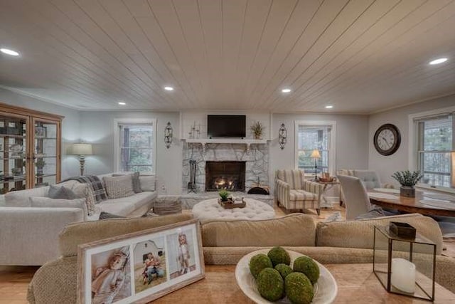 living room featuring wood ceiling, ornamental molding, a stone fireplace, and light hardwood / wood-style floors