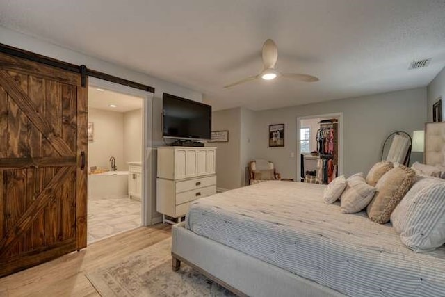 bedroom with ensuite bath, a barn door, a walk in closet, a closet, and light wood-type flooring