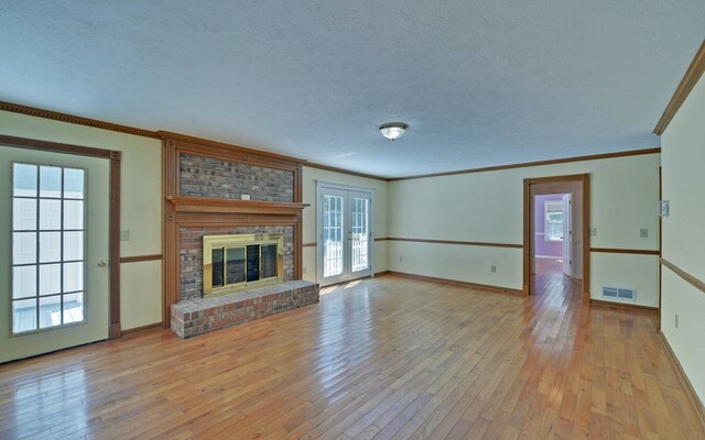 unfurnished living room featuring a brick fireplace, a wealth of natural light, light hardwood / wood-style floors, and a textured ceiling