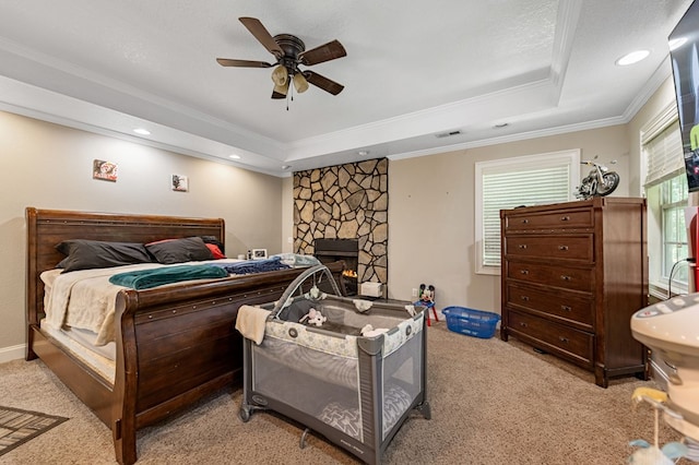 bedroom with a fireplace, a raised ceiling, ceiling fan, crown molding, and light colored carpet