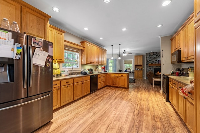 kitchen with a stone fireplace, black appliances, kitchen peninsula, ceiling fan, and pendant lighting