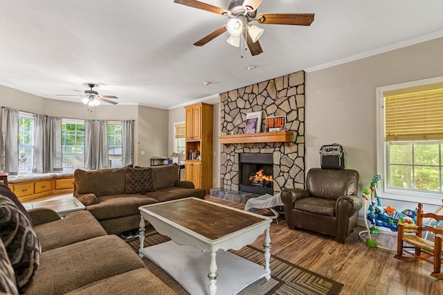 living room featuring light wood-type flooring, ceiling fan, crown molding, and a stone fireplace