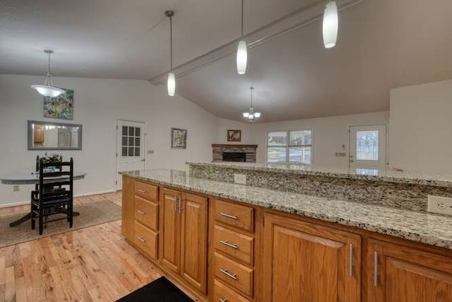 kitchen featuring light wood-type flooring, light stone counters, a fireplace, vaulted ceiling with beams, and decorative light fixtures