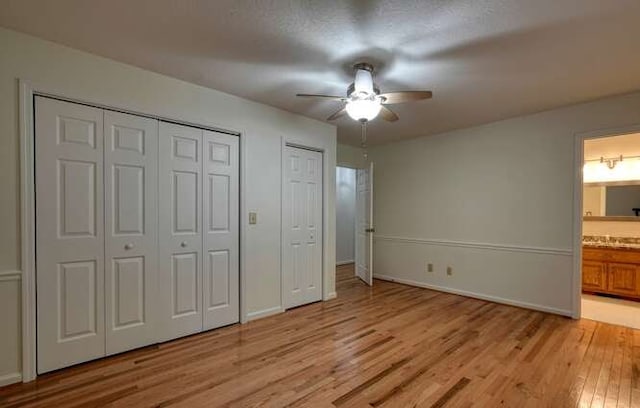 unfurnished bedroom with ceiling fan, a textured ceiling, light hardwood / wood-style flooring, two closets, and ensuite bathroom