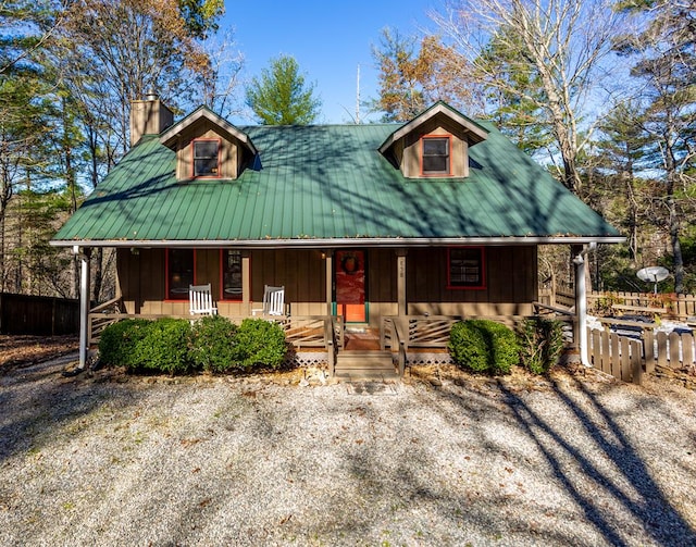 view of front facade with covered porch, a chimney, and fence