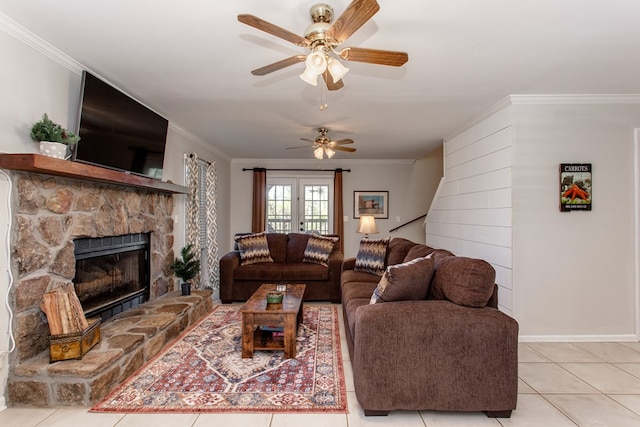 living room with baseboards, ornamental molding, a stone fireplace, light tile patterned flooring, and a ceiling fan