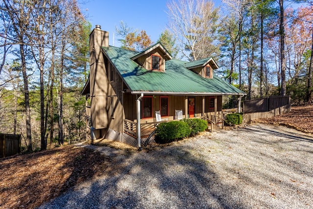 view of front of home with metal roof, covered porch, a chimney, and fence