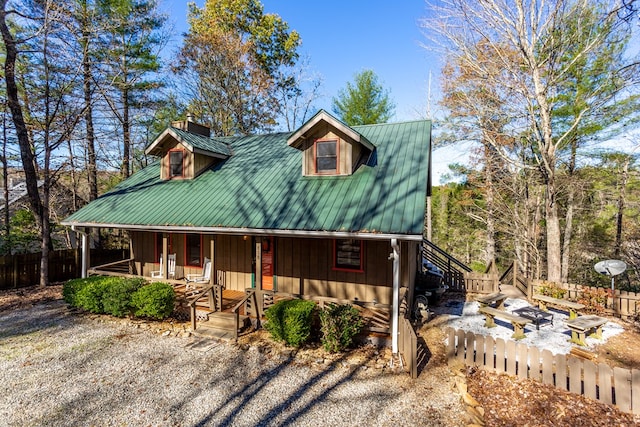 view of front facade with metal roof, a porch, a chimney, and fence