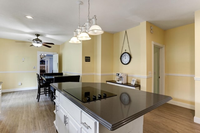 kitchen featuring black electric cooktop, dark countertops, light wood-style flooring, and ceiling fan with notable chandelier