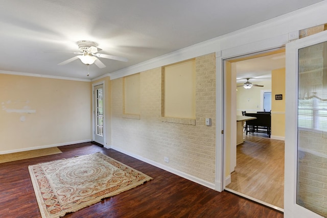 spare room with brick wall, baseboards, ceiling fan, ornamental molding, and wood finished floors