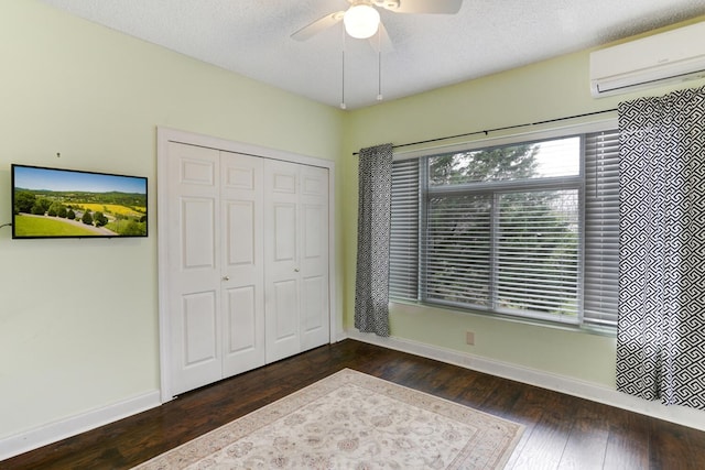 unfurnished bedroom with baseboards, a wall mounted air conditioner, a closet, a textured ceiling, and wood-type flooring