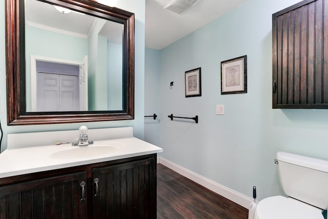 half bath with vanity, wood finished floors, baseboards, visible vents, and toilet