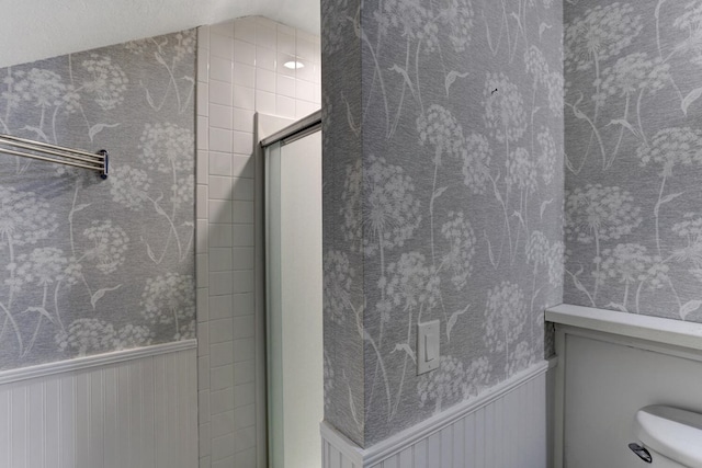 bathroom featuring a shower with door, a wainscoted wall, toilet, and lofted ceiling