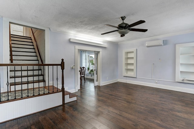 empty room featuring a wall unit AC, built in features, ornamental molding, wood-type flooring, and a textured ceiling