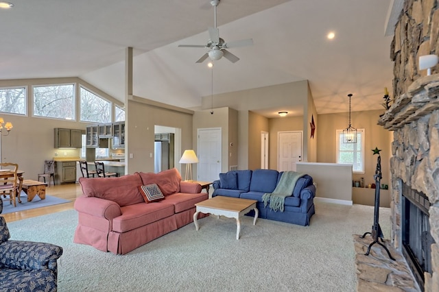 carpeted living room with plenty of natural light, a stone fireplace, ceiling fan with notable chandelier, and high vaulted ceiling