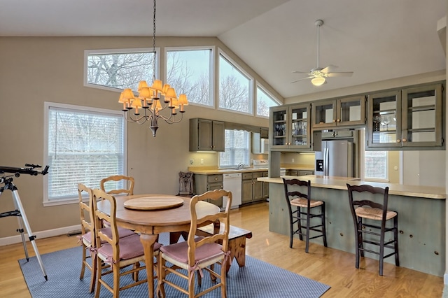 dining space with ceiling fan with notable chandelier, light hardwood / wood-style floors, high vaulted ceiling, and sink