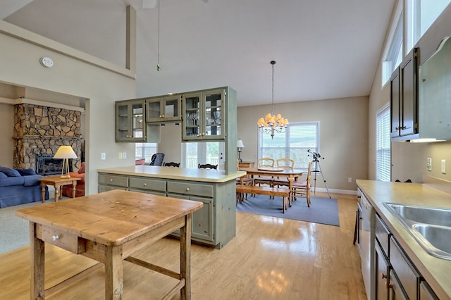 kitchen featuring pendant lighting, a stone fireplace, sink, a notable chandelier, and light hardwood / wood-style floors