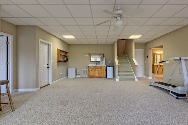 interior space with a paneled ceiling, light colored carpet, and ceiling fan