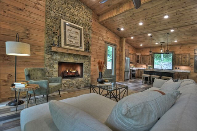 living room featuring wooden ceiling, hardwood / wood-style floors, a stone fireplace, wood walls, and vaulted ceiling with beams