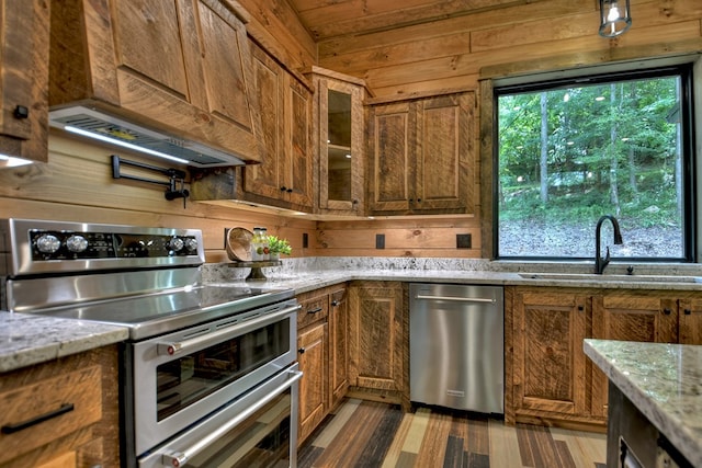 kitchen with wood walls, light stone counters, stainless steel appliances, and sink