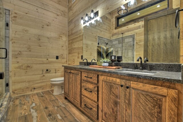 bathroom featuring vanity, a shower with shower door, hardwood / wood-style floors, toilet, and wooden walls