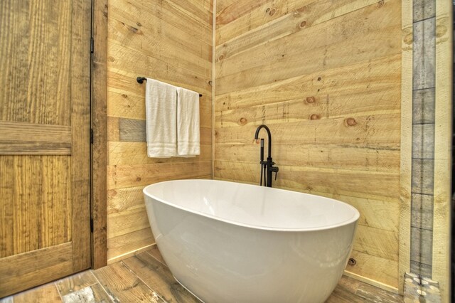 bathroom featuring wood walls, hardwood / wood-style floors, and a bathing tub