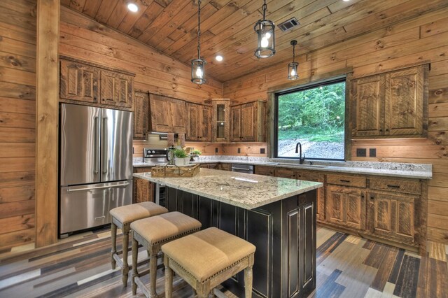 kitchen featuring light stone counters, a center island, sink, appliances with stainless steel finishes, and lofted ceiling