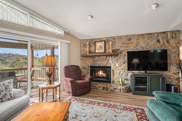 living room with vaulted ceiling, a stone fireplace, a textured ceiling, and wood finished floors