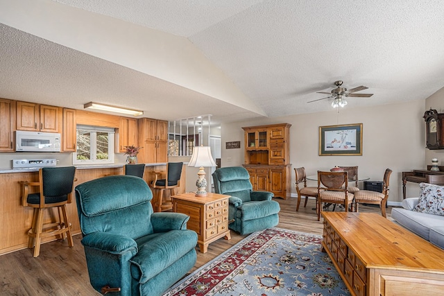 living area with vaulted ceiling, ceiling fan, a textured ceiling, and wood finished floors