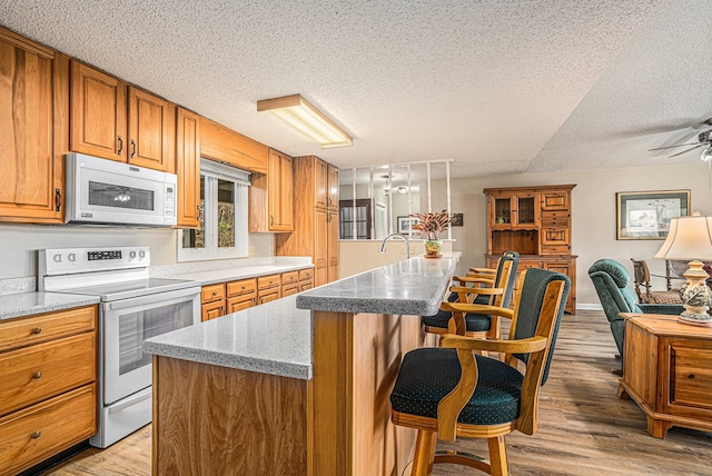 kitchen featuring white appliances, brown cabinets, a breakfast bar, a kitchen island with sink, and light wood-style floors