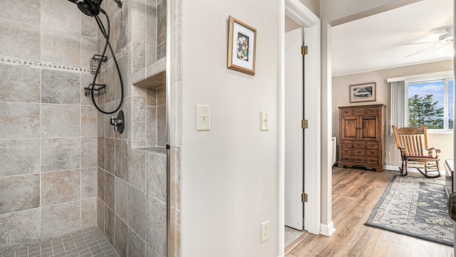 full bath featuring ceiling fan, a tile shower, baseboards, and wood finished floors