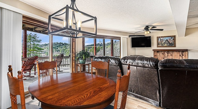 dining room with light wood-type flooring, a wealth of natural light, a textured ceiling, and ceiling fan with notable chandelier