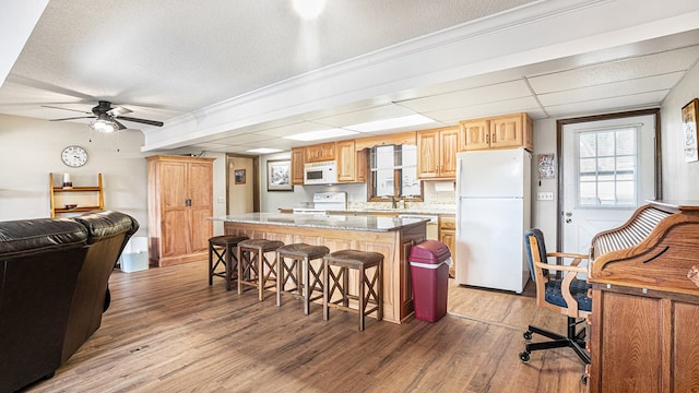 kitchen featuring a center island, a breakfast bar area, light brown cabinets, wood finished floors, and white appliances