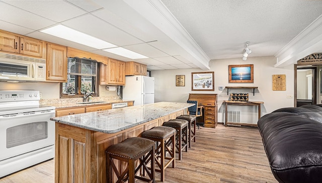 kitchen with light wood finished floors, a breakfast bar area, open floor plan, a sink, and white appliances