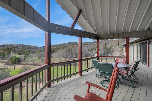 deck with a forest view and outdoor dining area