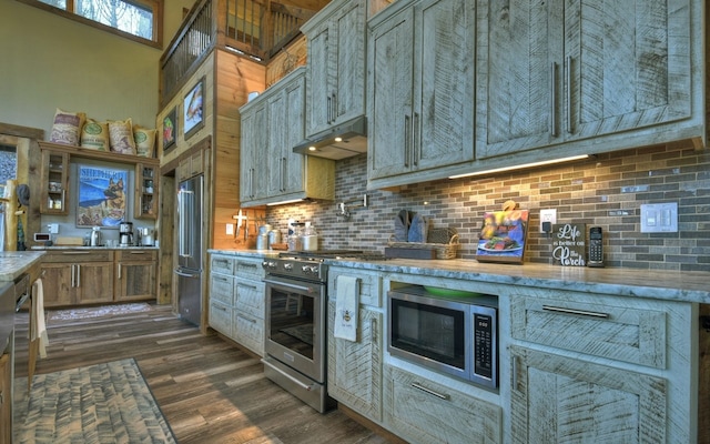 kitchen featuring dark wood-style floors, light stone counters, under cabinet range hood, high quality appliances, and tasteful backsplash