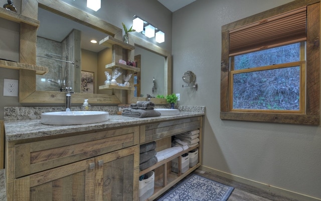 full bath with double vanity, wood finished floors, a sink, baseboards, and a shower