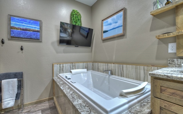 bathroom with a garden tub, wood finished floors, and vanity