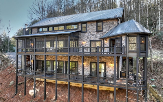 back of property with a balcony, a sunroom, stone siding, and metal roof