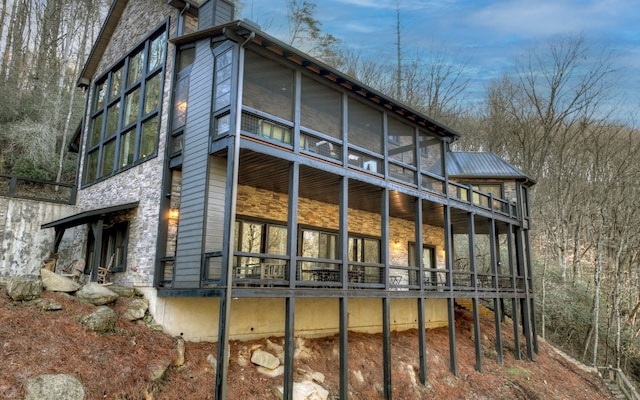 back of house with stone siding and a sunroom